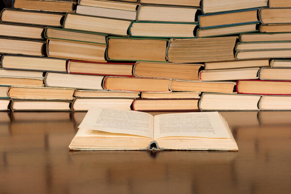 Открытая книга на столе на фоне книжных стопок

