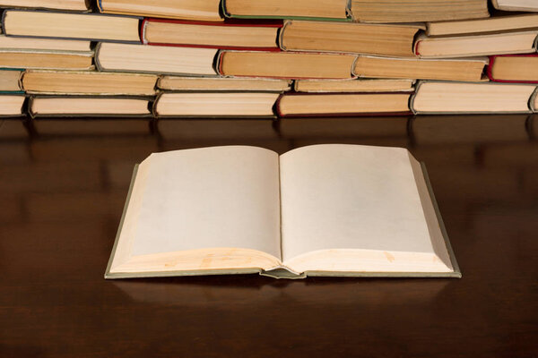 Open blank book on the desk with background of book piles