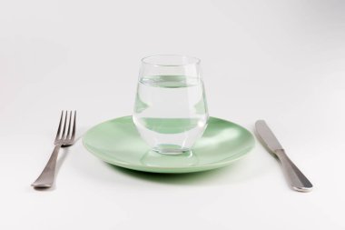 glass of water in a plate with knife and fork isolated on white background clipart