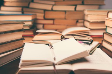 Eğitim kavramı açık kitap ve masanın üstünde defter ile öğrenme. Kitap okuma Resepsiyon ve gözlük kitap rafı arka planda yığınları yığını