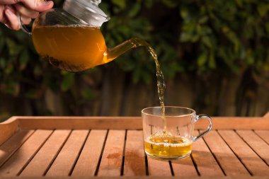 Doğanın bulanık arka planında çaydanlıktan bir fincana çay dökmek