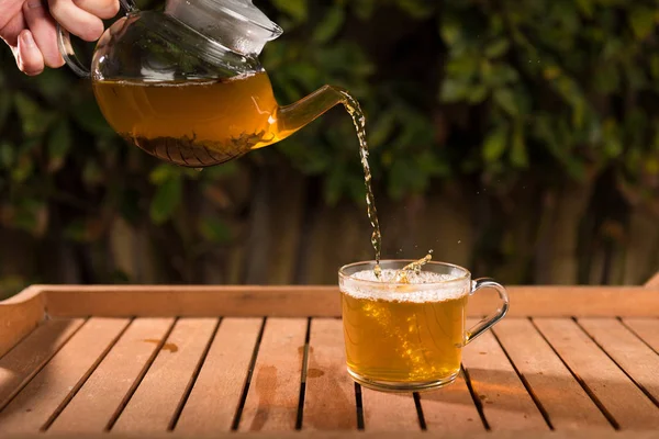 急須から茶を自然を背景にぼかしたカップに入れる — ストック写真