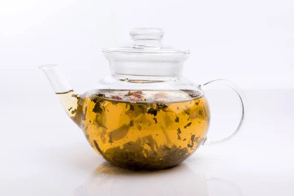 Glass teapot with herbal tea and roses isolated on white background