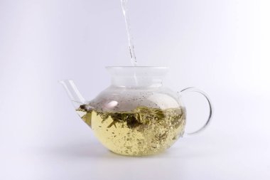 Bitkisel çay, beyaz arka plan üzerinde izole ile cam çaydanlık için sıcak su dökerek