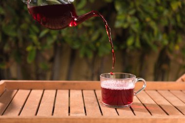 Doğanın bulanık arka planında çaydanlıktan bir fincana çay dökmek