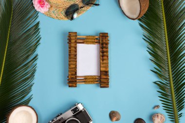 Fotoğraf çerçevesi, yeşil yapraklar, mavi pastel arka plan üzerinde şapka ve güneş gözlüğü ile şık yaz kompozisyon. Kopyalama alanı ile resim maket