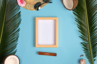 Fotoğraf çerçevesi, yeşil yapraklar, mavi pastel arka plan üzerinde şapka ve güneş gözlüğü ile şık yaz kompozisyon. Kopyalama alanı ile resim maket