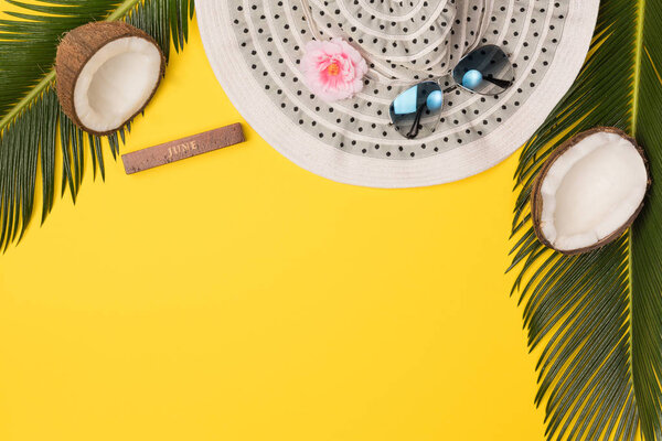 hat, coconuts and palm leaves isolated on yellow background, top view