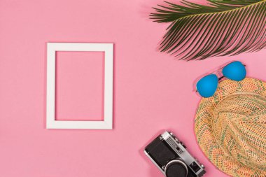 Pembe pastel arka plan üzerinde fotoğraf çerçevesi, yeşil yapraklar, şapka ve vintage fotoğraf makinesi ile şık yaz kompozisyonu. Kopyalama alanı ile resim maket