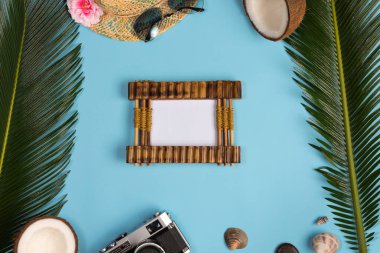 Fotoğraf çerçevesi, yeşil yapraklar, mavi pastel arka plan üzerinde şapka ve güneş gözlüğü ile şık yaz kompozisyon. Kopyalama alanı ile resim maket