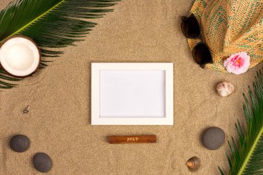 Fotoğraf çerçevesi, yeşil yaprakları, şapka ve kum arka plan üzerinde güneş gözlüğü ile şık yaz kompozisyon. Kopya alanı ile sanat mockup
