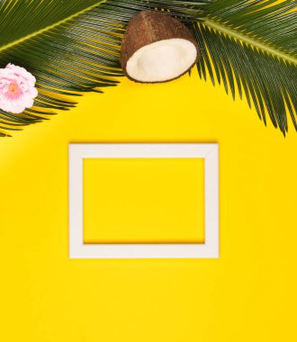 Fotoğraf çerçevesi, yeşil yaprakları, hindistan cevizi ve çiçek sarı bir arka plan üzerinde şık yaz kompozisyon. Resim kopyalama alanı ile mockup. Kare görüntü