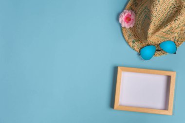 Mavi pastel arka plan üzerinde fotoğraf çerçevesi, şapka ve güneş gözlüğü ile şık yaz kompozisyonu. Kopyalama alanı ile resim maket