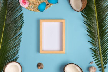 Fotoğraf çerçevesi, yeşil yapraklar, mavi pastel arka plan üzerinde şapka ve güneş gözlüğü ile şık yaz kompozisyon. Kopyalama alanı ile resim maket