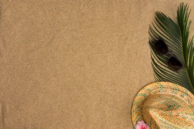 Metin için alan, kum arka plan üzerinde plaj teması. Şapka, kum arka planda güneş gözlüğü. Üstte görüntü.