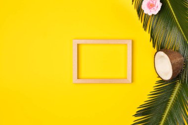 Fotoğraf çerçevesi, yeşil yaprakları, çiçek ve hindistan cevizi sarı bir arka plan üzerinde şık yaz kompozisyon. Kopyalama alanı ile resim maket