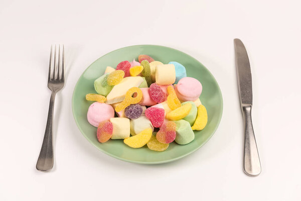 Вилка, нож и тарелка с зефиром и мармеладом конфеты изолированы на белом фоне. Вид сверху
.