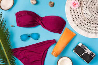 Mavi arka planda plaj teması. Güneş gözlüğü, şapka, güneş kremi, mayo, mavi arka planda. Üstte görüntü.