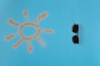 Güneş mavi arka plan üzerinde kum tarafından çizilmiş. Güneş gözlüğü mavi arka plan üzerinde izole. Üstte görüntü.