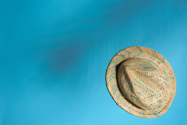 Straw hat and strong shadow of tropical palm leaves on  blue  background. Minimal summer concept. Top view.