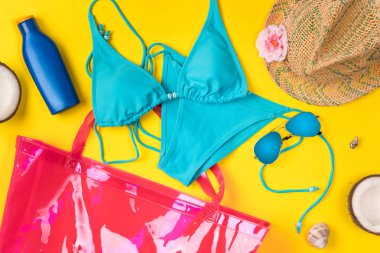 Sarı arka planda plaj teması. Plaj çantası, şapka, hindistan cevizi, mayo, sarı arka planda. Üstte görüntü.