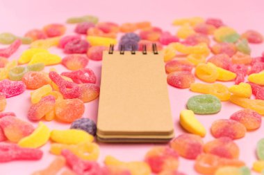 Şekerli jöle ve boş not defteri ile pembe kağıt arka plan. Metniniz için yerleştirin. Rahat tatlı arka plan