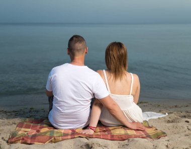 Aşık genç çift sahilde dinlenirken, kumda oturuyor.