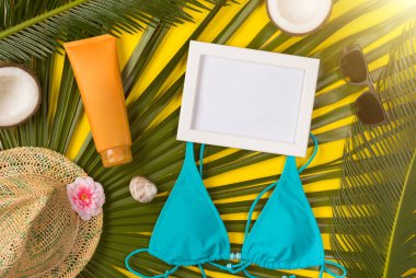 Sarı arka planda plaj teması. Plaj aksesuarları, palmiye yaprakları, sarı arka plan üzerinde fotoğraf çerçevesi. Üstte görüntü.