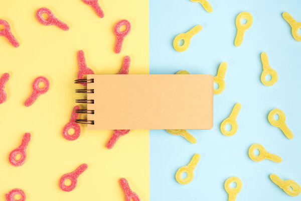 Откройте чистый блокнот на фоне конфет. Гамми конфеты на желтом и синем фоне. Вид сверху
.
