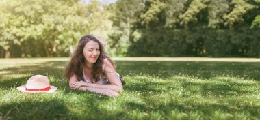 Güzel, gülümseyen kadın bir çim üzerinde, yeşil parkta yatıyor. 