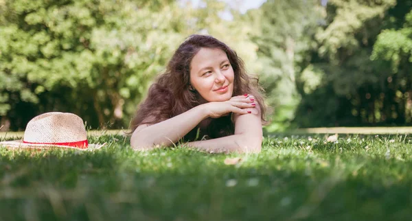 Beautiful, young girl dreaming on a grass, in summer park.