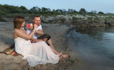 Plajda hamile çift, kum üzerinde oturan ve kavun yeme. 