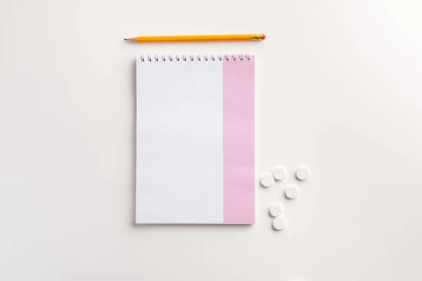 Notebook, pencil and  pills on white background. Flat lay.
