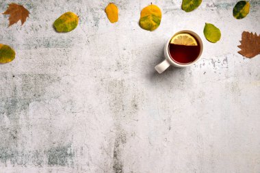 Sarı sonbahar yaprakları ile süslenmiş sıcak çay Fincan gri doku arka plan üzerinde bırakır. Düz yatıyordu