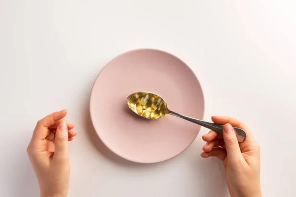 Hands with spoon of fish oil capsules. Flat lay.