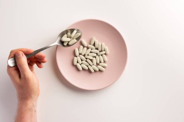 Erkek el hapları ile kaşık tutan. Haplarla kaplı tabak. Düz yatıyordu.