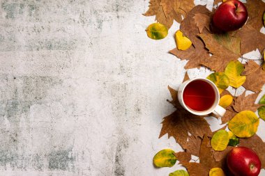 Sonbahar kompozisyonu. Kırmızı elma, bir fincan çay, yapraklar, gri beton arka plan üzerinde. Düz yatıyordu.