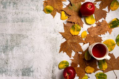 Sonbahar kompozisyonu. Kırmızı elma, bir fincan çay, yapraklar, gri beton arka plan üzerinde. Düz yatıyordu.
