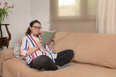 Kafkasyalı sakin bir kadın rahat bir kanepede kitap okuyor.