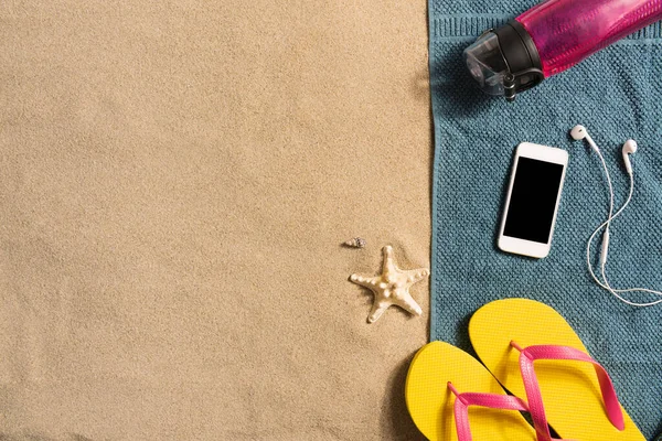 夏休みの構成 砂の背景に水のフリップフロップ スマートフォンやボトル 影の強い光 — ストック写真