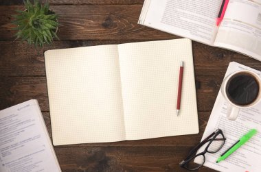 Bir fincan kahve, bardak, ev bitkisi ve ahşap arka planda boş bir not defteri olan açık bir kitabın en üst görüntüsü. İş yeri konsepti. Evde çalışıyorum.