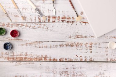 Sanatçının işyeri. Beyaz ahşap masadaki fırçalı boyalar ve boş tuvaller, üst manzara, düz yatış, nesneler