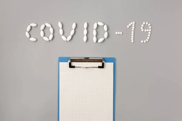COVID-19 flu epidemic. The inscription Covid-19 of pills.  Tablets and notepad on a gray background, Flat lay, copy space. Temperature measurment