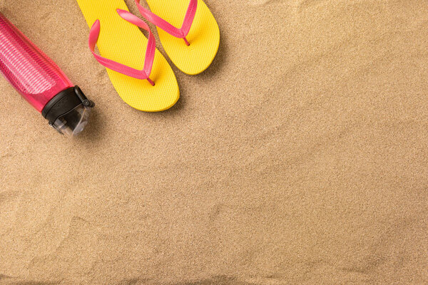 Top view flip flops and water bottle with copy space. Traveler accessories on sand. Travel vacation concept. Summer background. Border composition made of towel