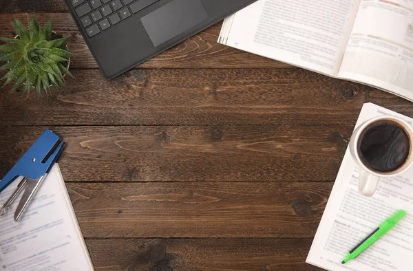 Flat lay, top view office table desk. Workspace with open books, laptop, office supplies, pencil, green highlighter, and coffee cup on wooden background