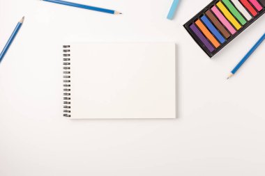 Renkli mum boya kalemleri, eskiz defteri beyaz arka planda izole edilmiş. Renkli tebeşir. Düz konum, üst görünüm, kopyalama alanı.