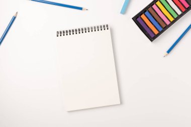 Renkli mum boya kalemleri, eskiz defteri beyaz arka planda izole edilmiş. Renkli tebeşir. Düz konum, üst görünüm, kopyalama alanı.
