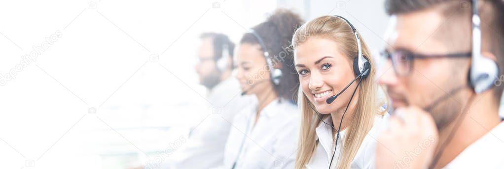 Call center worker accompanied by her team. Smiling customer support operator at work. Young employee working with a headset.