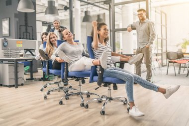 Rahat kılığına girmiş genç neşeli işadamları sandalye modern bir ofiste kürek üzerinde eğleniyor musun. Mutlu takım kavramı.