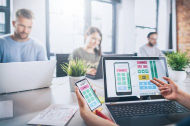 smartphone ve dizüstü bilgisayar, tasarımcılar erkek ve arka plan üzerinde ofiste çalışan kadın elle